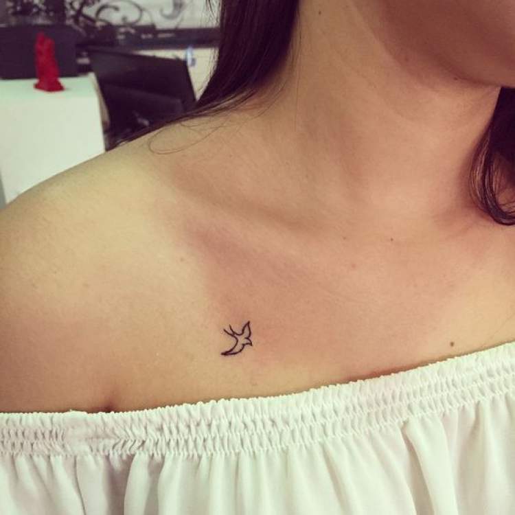 Tatuagem delicada de pássaro voando no colo ao lado do ombro