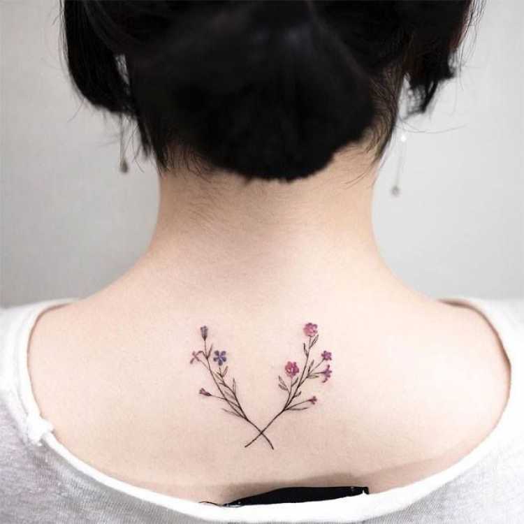 Tatuagem feminina com desenho de flores na parte superior central das costas próximo ao pescoço e nuca