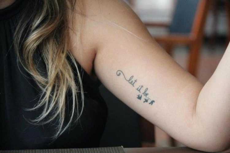 Tatuagem feminina delicada com dizeres na lateral do braço