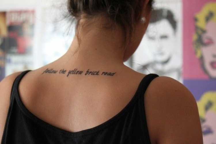 Tatuagem feminina com dizeres na parte superior das costas