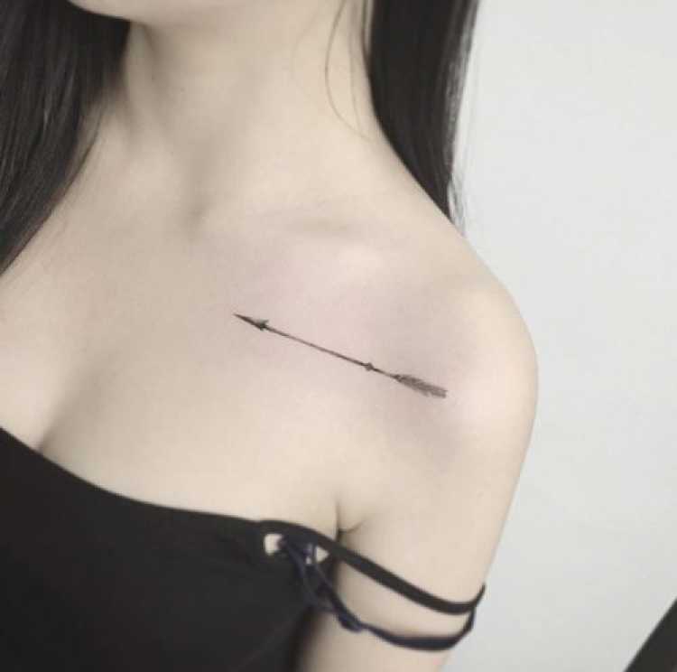 Tatuagem feminina delicada no peito na altura do ombro com o desenho de uma flecha
